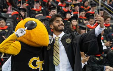 Graduation photo, student taking a selfie with Georgia Tech mascot, Buzz.